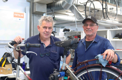 Twee fietsherstellers poseren bij een fiets in hun atelier.