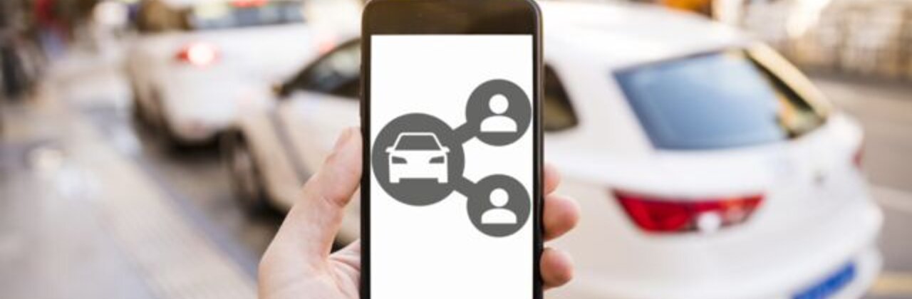 hand houd GSM vast met geparkeerde wagen in achtergrond