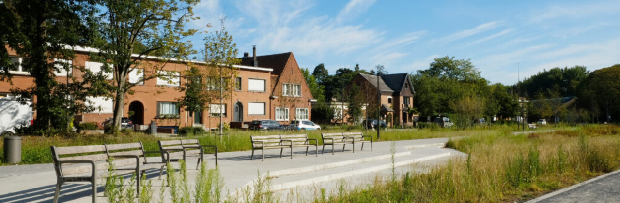 Zicht op inrit naar fort Mortsel met bankjes, gevels van huizen en groen