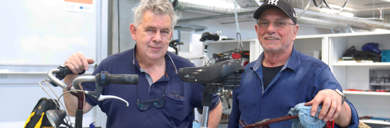 Twee fietsherstellers poseren bij een fiets in hun atelier.