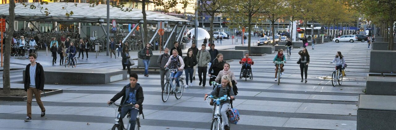 foto van winkelstraat met fietsers, voetgangers en geparkeerde wagens