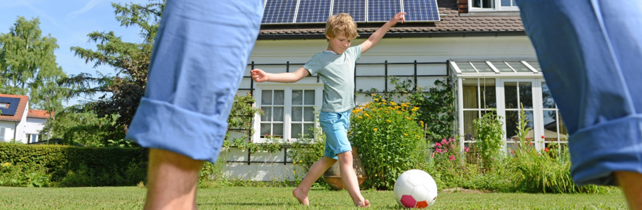 foto van tuin met spelende kinderen met woning met PV op de achtergrond