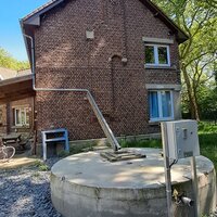 beeld van een afvoerpijp die regenwater naar een deels bovengrondse regenwaterput leidt