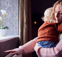 moeder met kind op de arm die voelt aan een radiator
