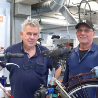 Twee fietsherstellers poseren bij een fiets in hun atelier.