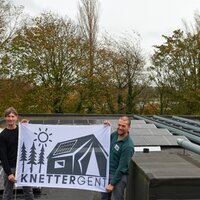 foto van PV-installatie op dak jeugdlokaal, met 2 mensen met vlag van Knettergent