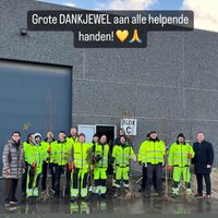 Groep mensen met fluovestjes aan die bomen vasthebben om te planten