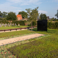 Begraafplaats met veel groen en grafstenen op de achtergrond.