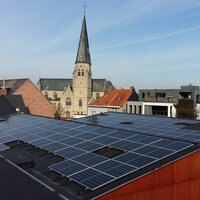 Dak met zonnepanelen met op achtergrond kerktoren Bonheiden. 