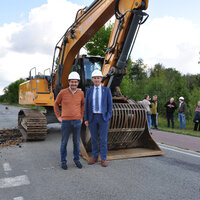 burgemeesters Wim Dries van stad Genk en Johny De Raeve van de gemeente Zonhoven poseren voor een graafmachine