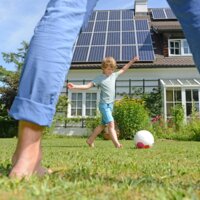 foto van tuin met spelende kinderen met woning met PV op de achtergrond